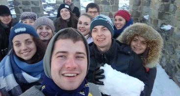 A happy selfie, taken by an international group at the top of the tower. The city is visible in the background. One of the boys is holding a snow lump.