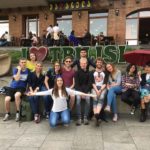 part of the group, cheerful as always, sits in front of the inscription "I love Tbilisi". Two girls hold an umbrella wide open above themselves.