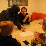 Четверо учасників сидять за столом та вивчають правила гри. Кожен тримає в руках декілька карт