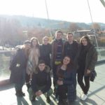 Група з 8 людей стоїть на відомому Мості Миру в Тбілісі. Яскраво світить сонце.