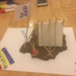 На столі лежить палатка, прапор та вогонь зроблені з допомогою пластиліну, паперу,паличок, та маркера. На прапорі намальований череп, а збоку ще один синьо-жовто-червоний прапор із написом “Bongalia”.