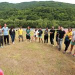 Учасники стоять у півколі. На фоні видніється річка та зелені гори.