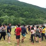 Учасники грають гру на поляні біля палаток та річки. Всі завмерли в різних позах.