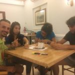 Чотири людини сидять за столом та будують палатку, використовуючи папір, пластилін, палички та маркери. Троє із них сконцентровані на роботі, четвертий дивиться на камеру та посміхається.