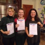 Three girls are standing next to each other, smiling and holding certificates in their hands